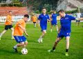 Fotbaliști în echipamente albastre și portocalii dispută mingea