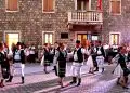 Dansatori în costume populare românești, în fața unei clădiri