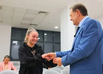 Bărbat în costum felicită o tânără într-o sală