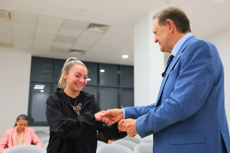 Bărbat în costum felicită o tânără într-o sală