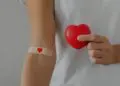 Persoană cu plasture cu inimă ține o inimă roșie