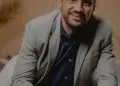 Bărbat zâmbitor cu ochelari, sacou gri și cămașă albastră