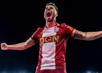 Fotbalist în tricou roșu sărbătorind cu brațele întinse