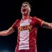Fotbalist în tricou roșu sărbătorind cu brațele întinse